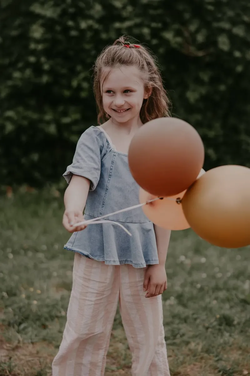 Mädchen lächelt und hält drei Luftballons in der Hand